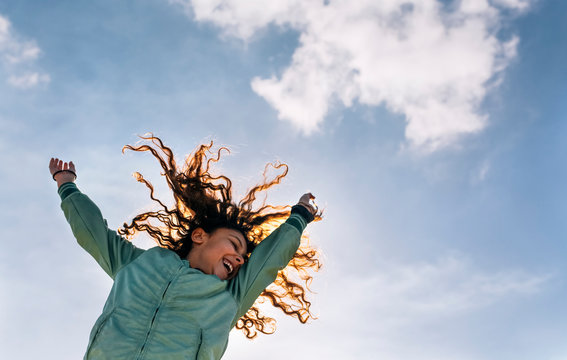Girl with arms raised jumping against sky
