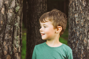 Portrait of a charming boy with a wide smile on the background of pine trees in forest