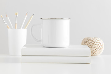Fototapeta na wymiar Enamel mug mockup with workspace accessories on a white table.