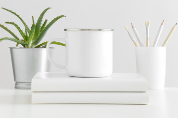 Fototapeta na wymiar Enamel mug mockup with workspace accessories and a succulent plant on a white table.