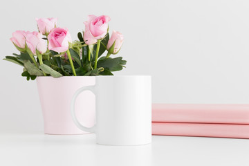 Mug mockup with books and pink roses in a pot on a white table.
