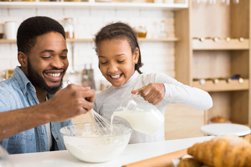 Smiling black girl pouring milk into dough bowl