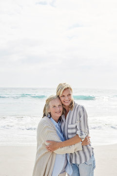 Senior Woman And Her Adult Daughter Standing On The Beach, Embracing