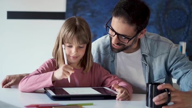 Handsome young father with his daughter drawing with digital tablet at home.