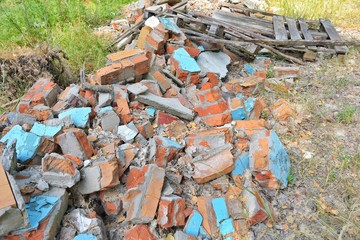 Pile of construction waste with old broken red bricks and broken boards. Rubbish from a ruined house with bricks pieces and old timber. Junk yard outdoor. Old building materials polluting environment