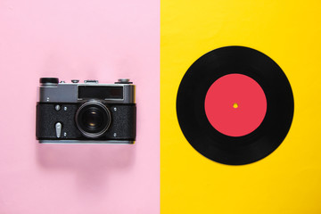 Retro still life, 70s. Vinyl record and film camera on pink yellow background. Top view. Flat lay