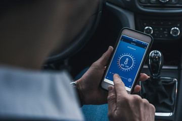 Man in car adjusting smart home device via smartphone