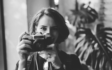 Portrait of a stylish hipster woman with a short haircut with retro camera takes a picture indoors