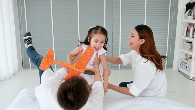 Asian family happy spending time together in the house. Father, mother and daughter aged three enjoying playing a plane on the bed. Slow motion