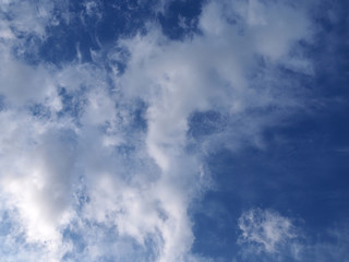 Landscape of beautiful blue sky covered with light thin fluffy white clouds and a thundercloud coming from the left with the sun illuminates the lower part of the clouds. Natural blue sky on day time 