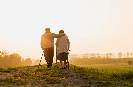 Senior couple walking with walking stick and wheeled walker in the nature