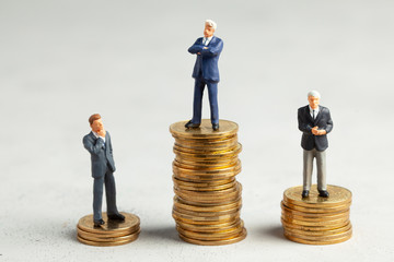 Successful businessman with big profits on stack of gold coins and less successful businessmen with small companies. Adequate investment in the company.