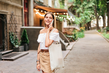 Fototapeta premium Cheerful charismatic woman talking on the phone while walking in the evening along the old city street