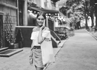 Cheerful charismatic woman talking on the phone while walking in the evening along the old city street
