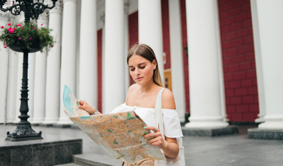 Young beauty woman tourist explore city map in urban environment against the background of columns