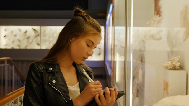 Teenager cute girl makes draw sketches in graphic tablet of stuffed animals and birds in museum of nature as part of school task of biology