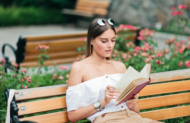 Obraz premium Young blonde woman reading a book with enthusiasm while sitting on a bench in a park