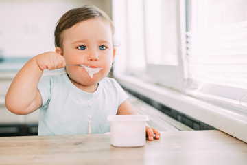Little girl in the afternoon in the kitchen eating yogurt