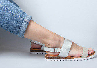 Female legs in jeans and trendy sandals sitting on white background. Cropped Studio Shot