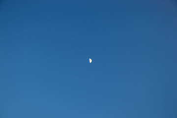 Half of the moon on a clear blue sky in the afternoon. A small satellite of the earth ra monophonic background.