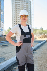 Portrait of young handsome hard worker wearing white protective helmet and working overalls at concstruction site