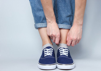 Fashionable studio shot. Woman in jeans and sneakers pops a sock on gray background.