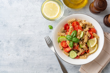 Whole wheat pasta salad with cucumbers, cherry tomatoes, salted salmon and capers on concrete background. Top view. Copy space.