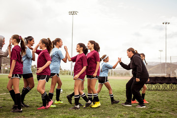 Sports teams with coaches doing high-five on field against sky during soccer match © Cavan for Adobe
