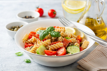 Whole wheat pasta salad with cucumbers, cherry tomatoes, salted salmon and capers on concrete background. Selective focus.