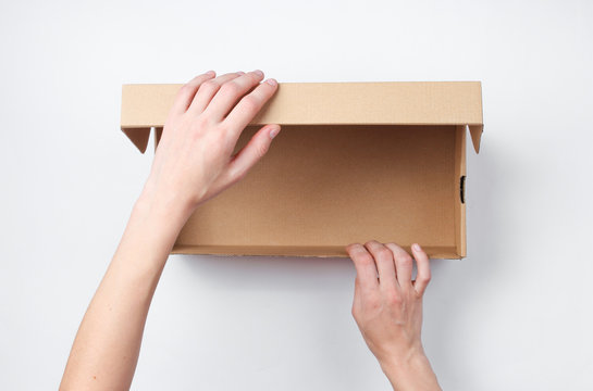 Female hands open empty cardboard box on gray background. Top view