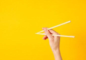 Female hand hold chopsticks on yellow background. Minimalistic food concept. Top view