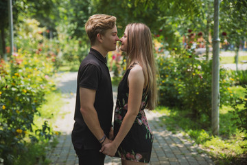 Fototapeta premium A couple of teenagers in love hugs and poses against the background of flowering trees and shrubs. Young guy and girl on the background of a blooming Park