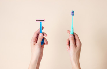 Personal care. Female hands holding a toothbrush and a razor on a beige background. Top view