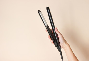 Hair care. Female hand holding hair straightener on a beige background. Top view