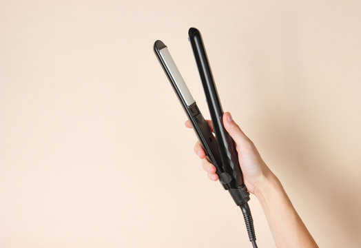 Hair care. Female hand holding hair straightener on a beige background. Top view