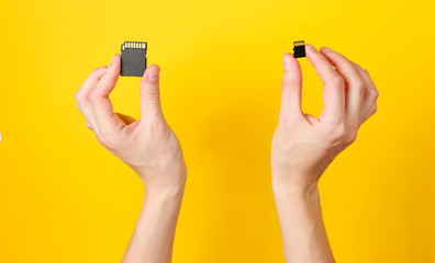 Female hands holds two SD memory cards on yellow background. Minimalist Techno Concept. Top view