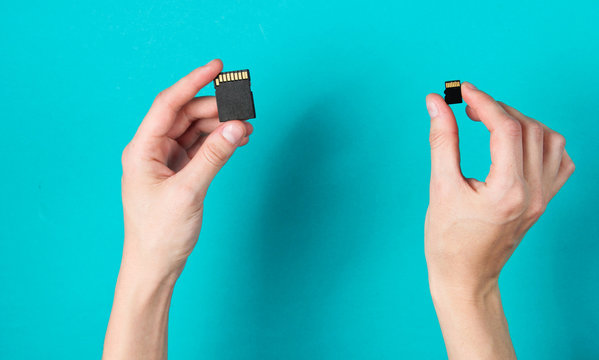 Female hands holds two SD memory cards on blue background. Minimalist Techno Concept. Top view