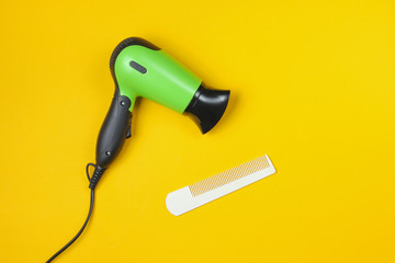 Minimalistic beauty and fashion still life. Hair dryer and comb on yellow background. Top view,...
