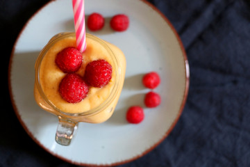 Mango and banana smoothie decorated with raspberries and reusable straw. Top view.