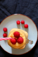 Mango and banana smoothie decorated with raspberries and reusable straw. Top view.