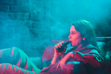 woman smokes a e-cigarette lying on the bed in the room. Smoker's concept Vaping.