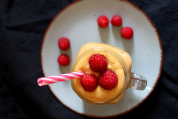 Mango and banana smoothie decorated with raspberries and reusable straw. Top view.