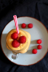 Mango and banana smoothie decorated with raspberries and reusable straw. Top view.
