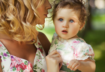 People and family concept - Close up portrait of a mother and little daughter with blue eyes in summer park against a background of green grass