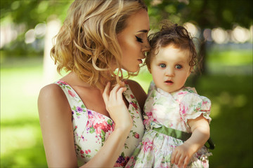 People and family concept - Close up portrait of a mother and little daughter with blue eyes in summer park against a background of green grass and trees