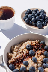 Oatmeal with blueberies and cocoa powder in a round bowl and cup of black coffee.