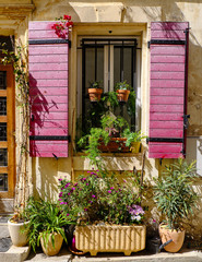 Fototapeta na wymiar Typical Provence window with red shutters, overloaded with flower pots and bright sunny day