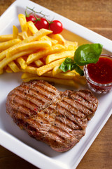 Grilled steak, fries, sauce and vegetables on plate