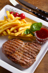 Grilled steak, fries, sauce and vegetables on plate
