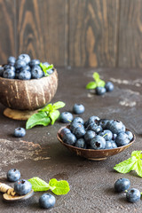 Freshly picked blueberries in wooden bowl. Juicy and fresh blueberries with mint on dark stone background. Blueberry antioxidant. Concept for healthy eating and nutrition. 